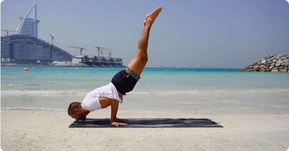 Mohammed F. Mostafa in a forearm stand on the beach, Burj Al Arab behind him
