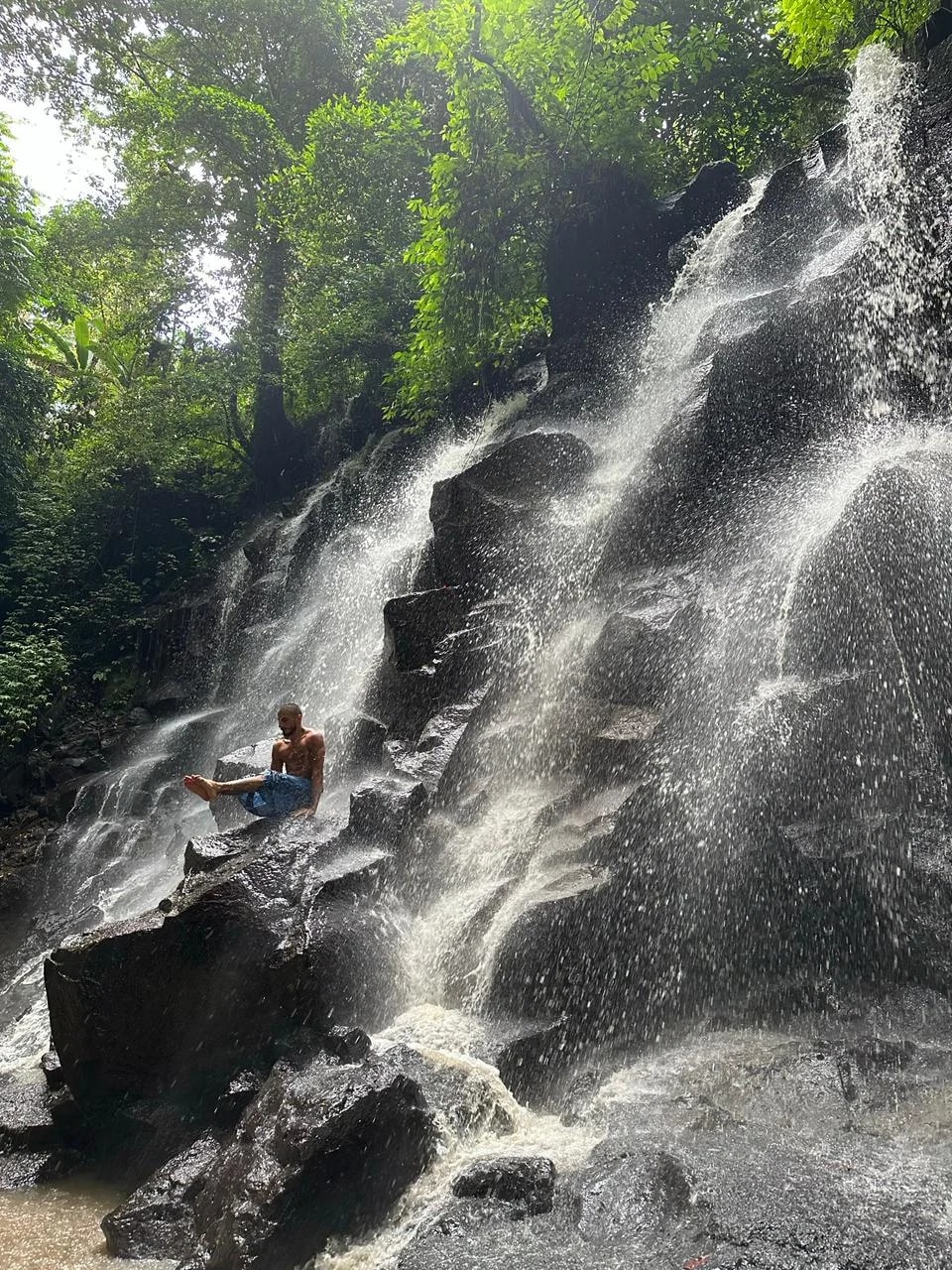 A man sitting on rocks beneath a jungle waterfall
